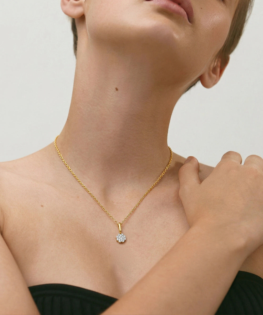 Gold necklace with a diamond pendant worn by a person against a neutral background