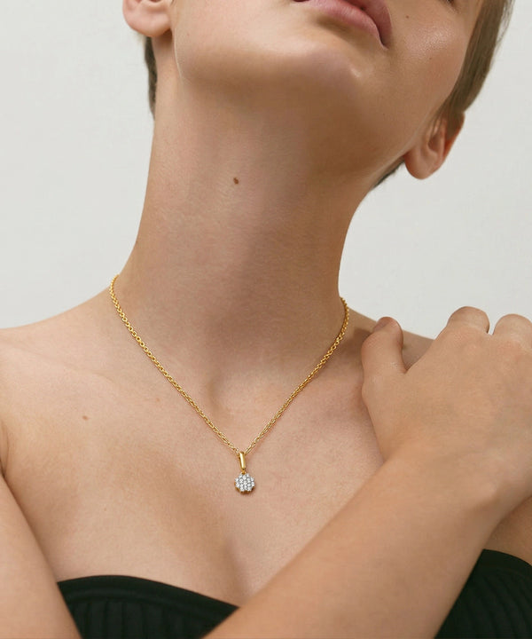 Gold necklace with a diamond pendant worn by a person against a neutral background