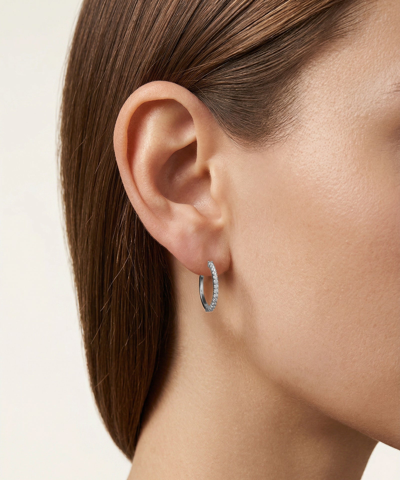 Close-up of a person wearing a silver hoop earring with a plain background
