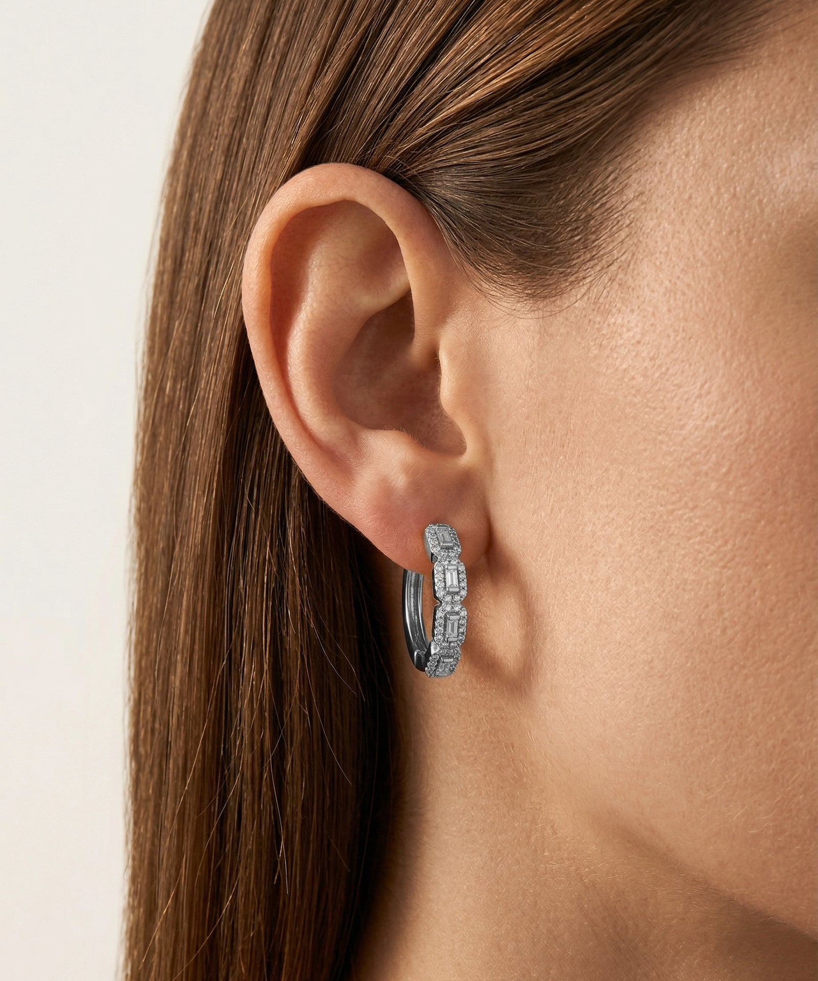 Close-up of an ear wearing a diamond earring with a neutral background