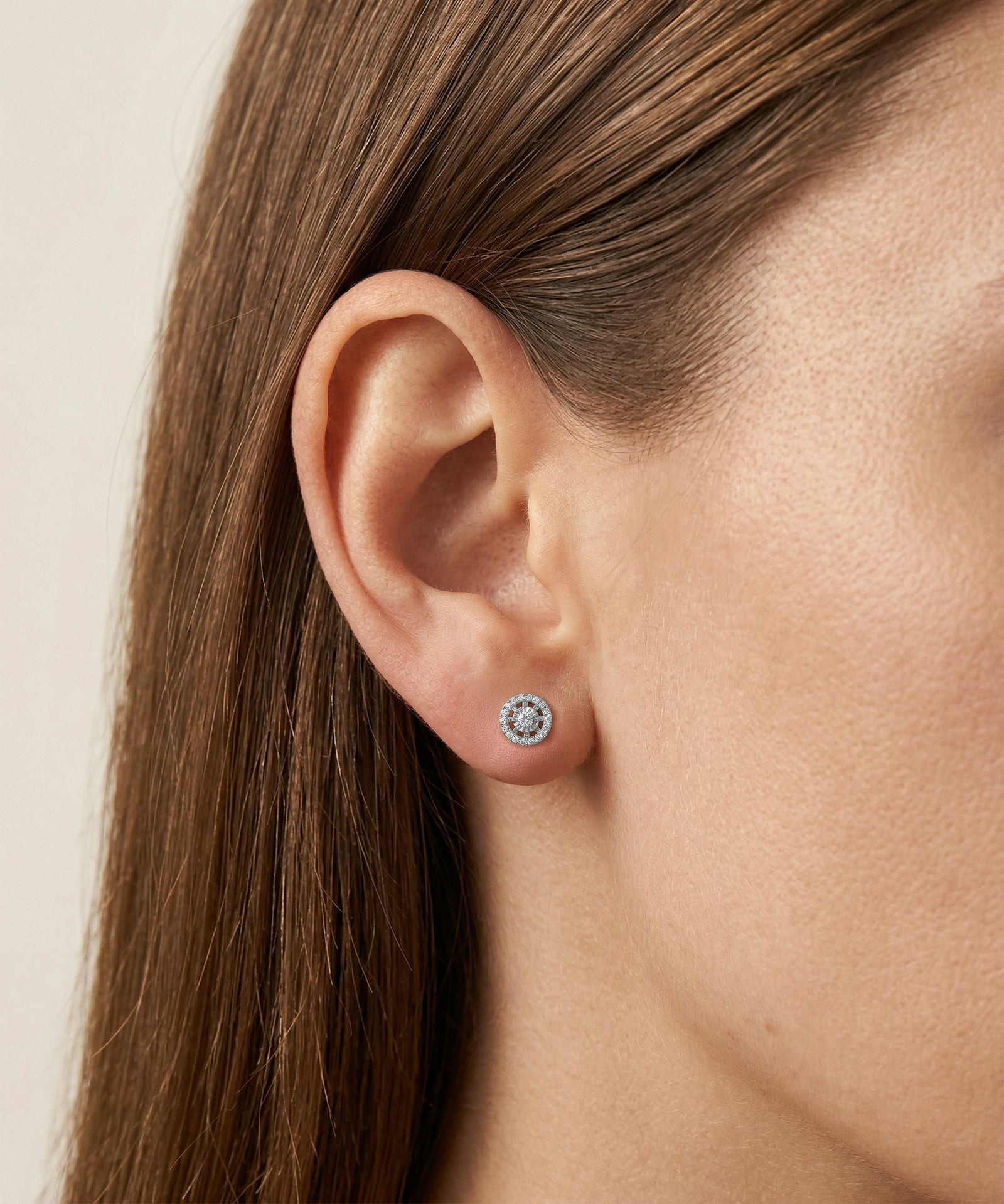 Close-up of an ear wearing a diamond stud earring with a neutral background