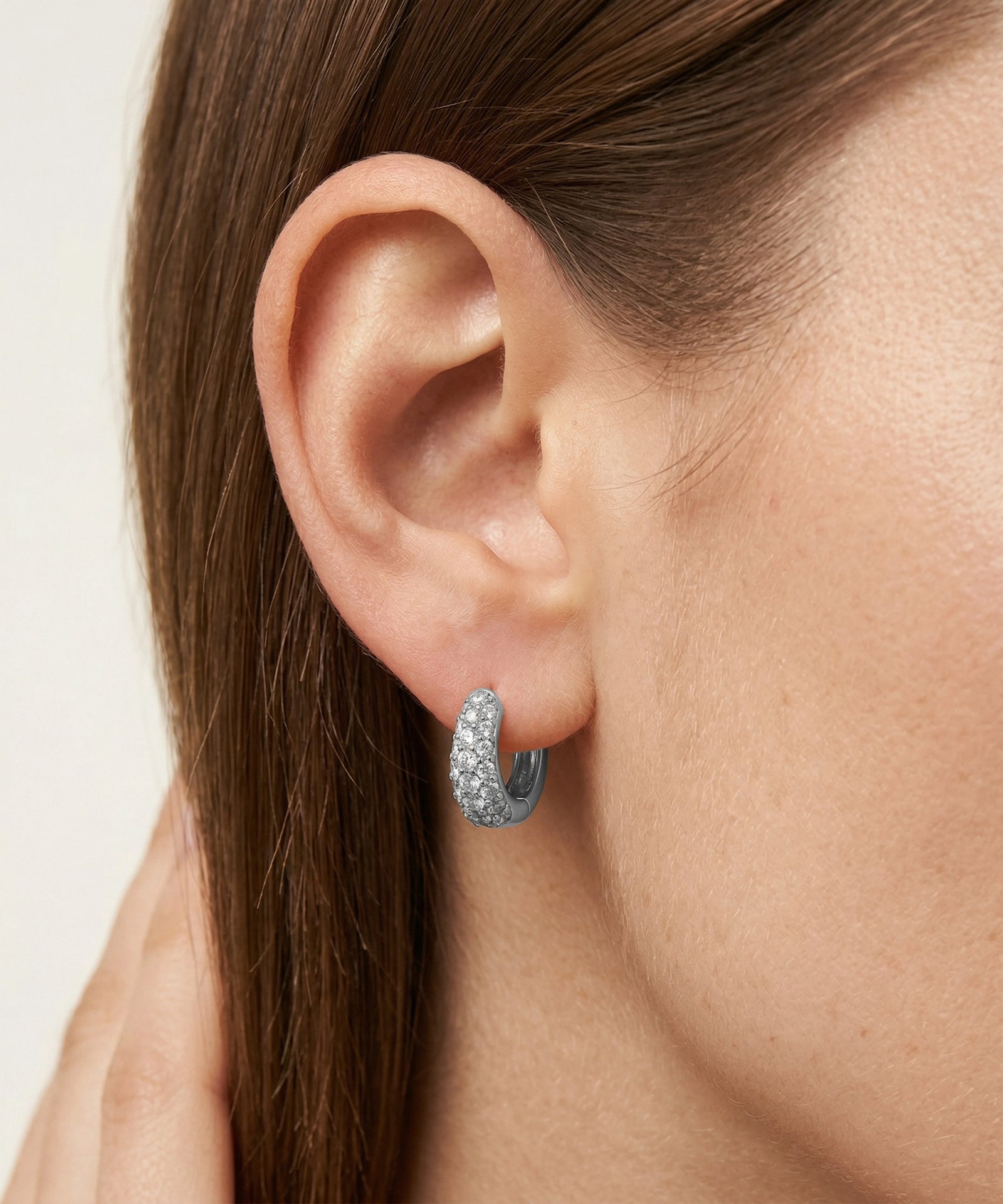 Close-up of a woman's ear wearing a silver hoop earring with clear stones.