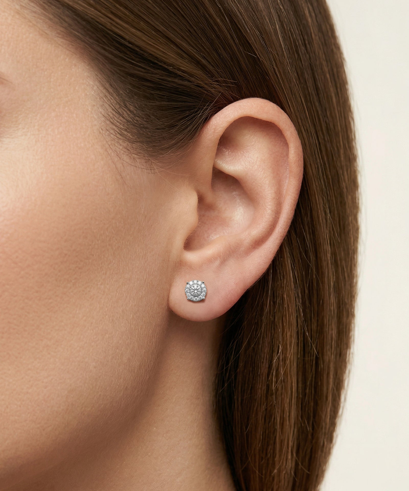 Close-up of an ear wearing a silver earring with a clear gemstone on a neutral background