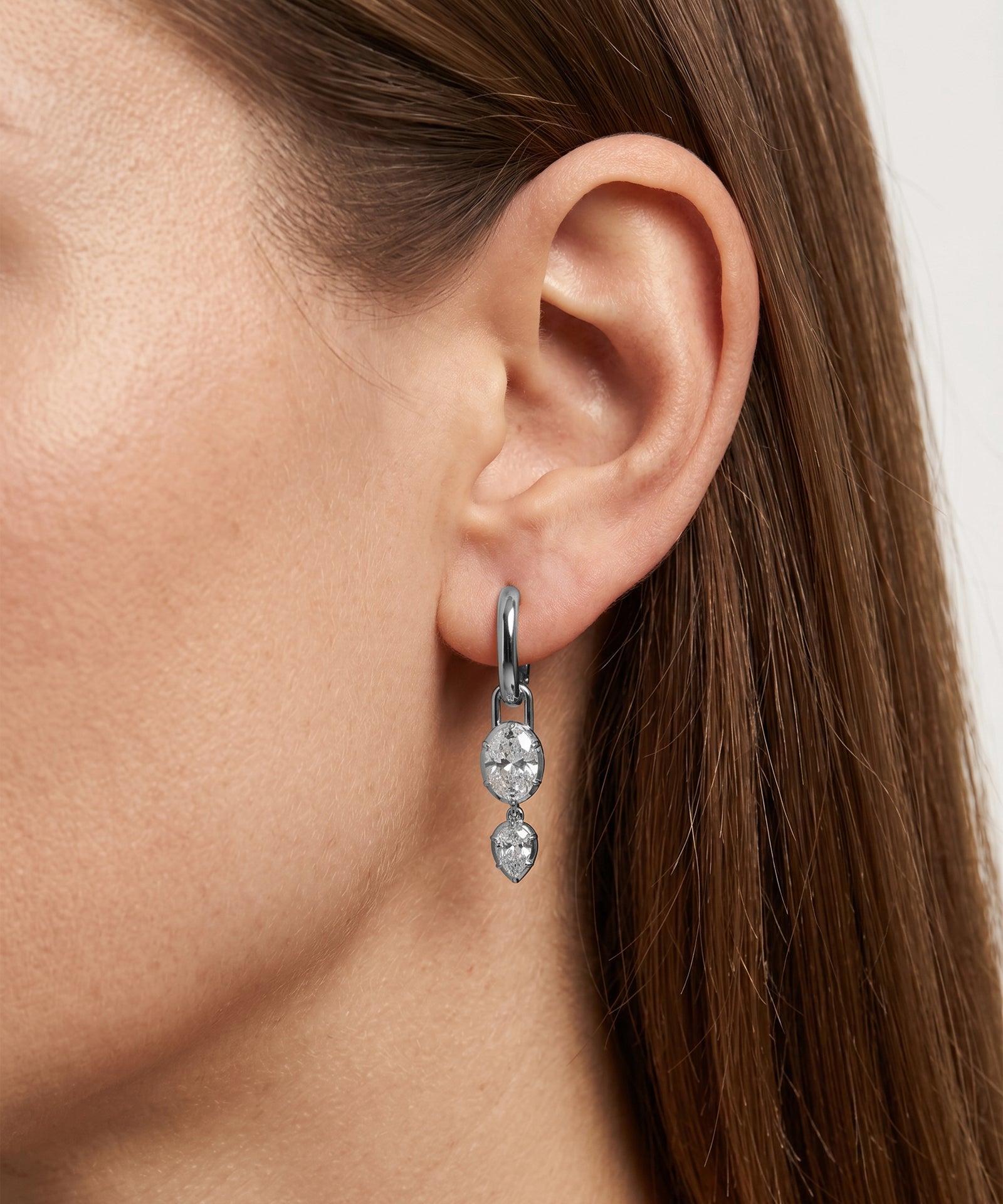 Close-up of a person wearing a silver earring with a clear gemstone.