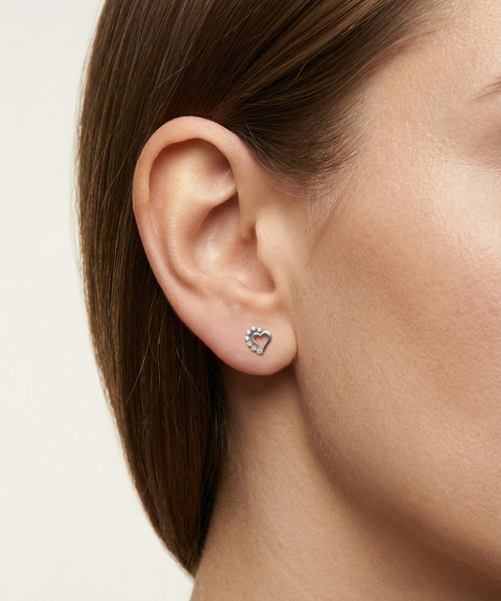 Close-up of an ear wearing a heart-shaped earring with small stones on a neutral background