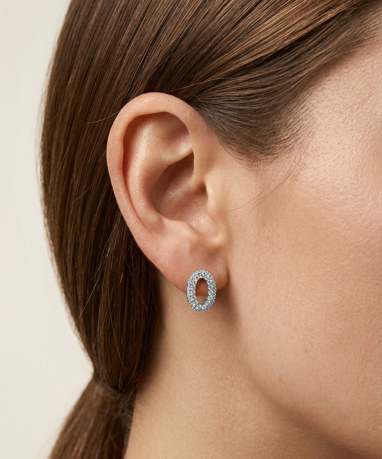 Close-up of an ear wearing a diamond hoop earring with a neutral background
