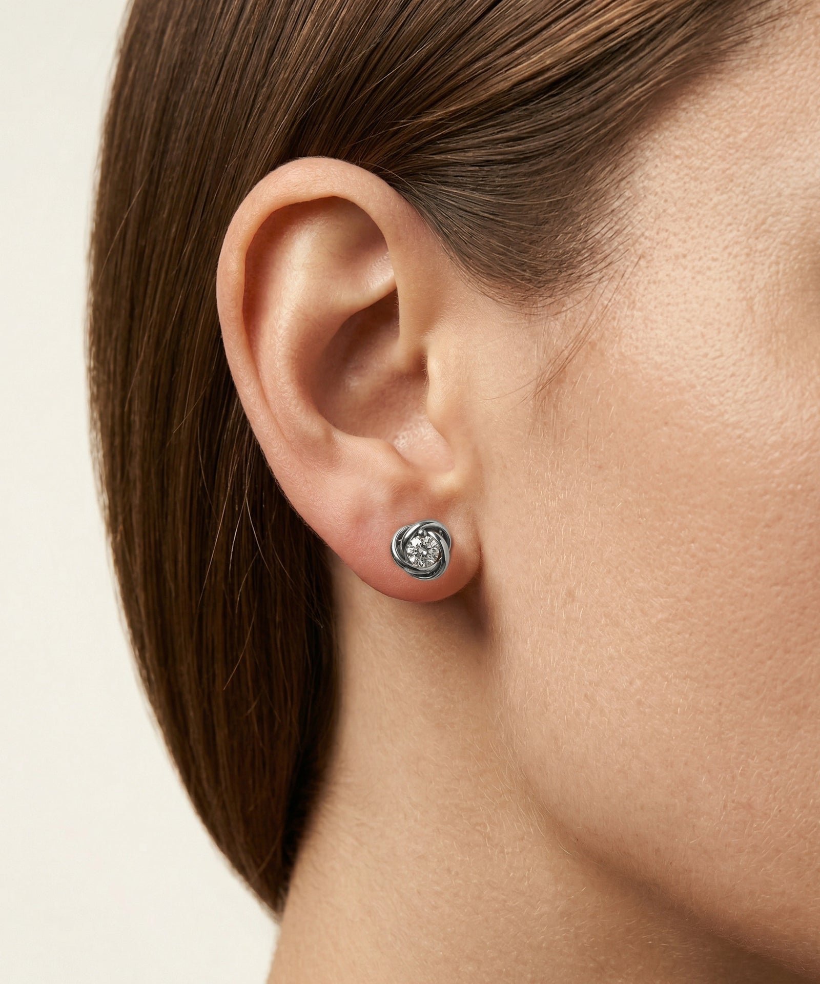 Close-up of an ear wearing a diamond stud earring on a neutral background