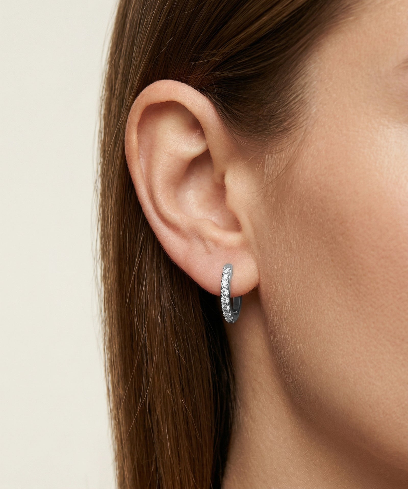 Close-up of an ear wearing a silver hoop earring on a neutral background