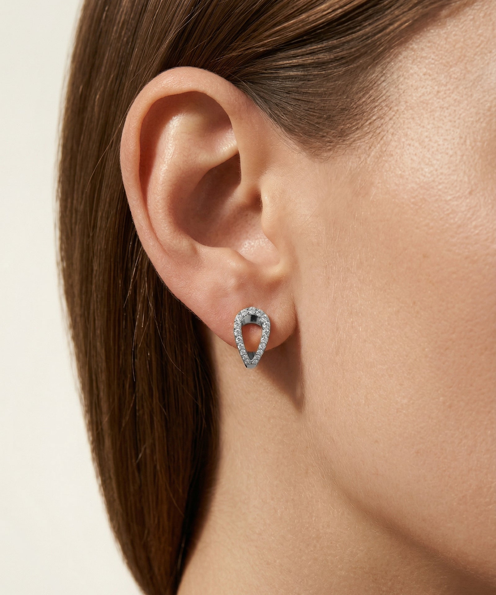 Close-up of an ear wearing a silver earring with a light background