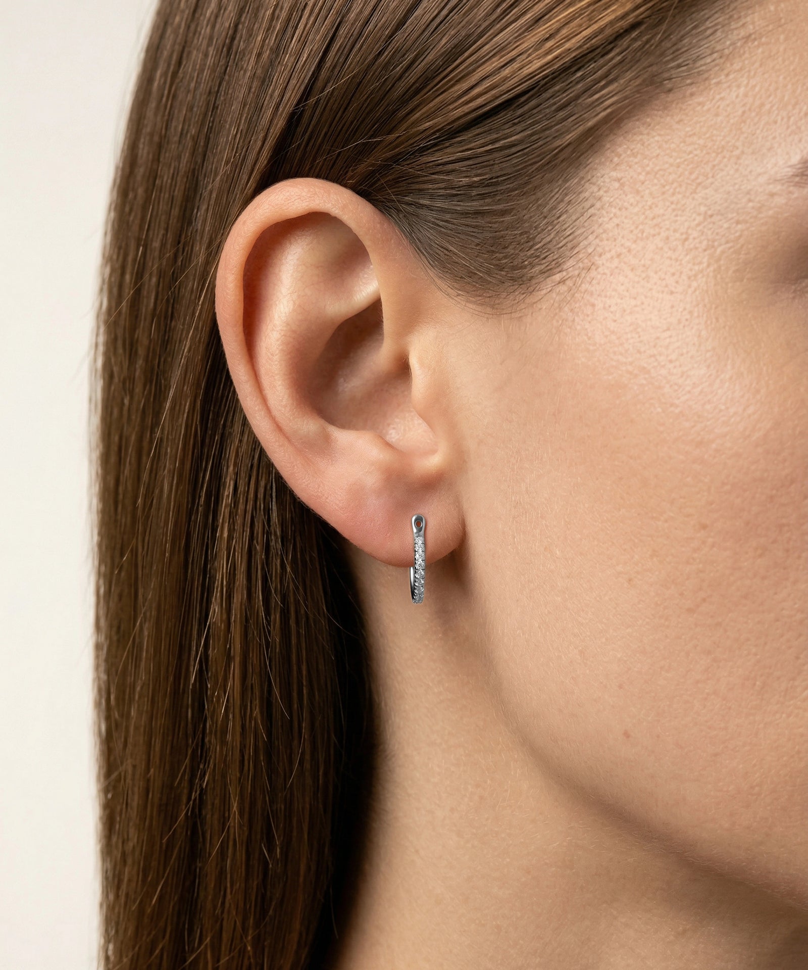 Close-up of an ear wearing a silver hoop earring with a neutral background