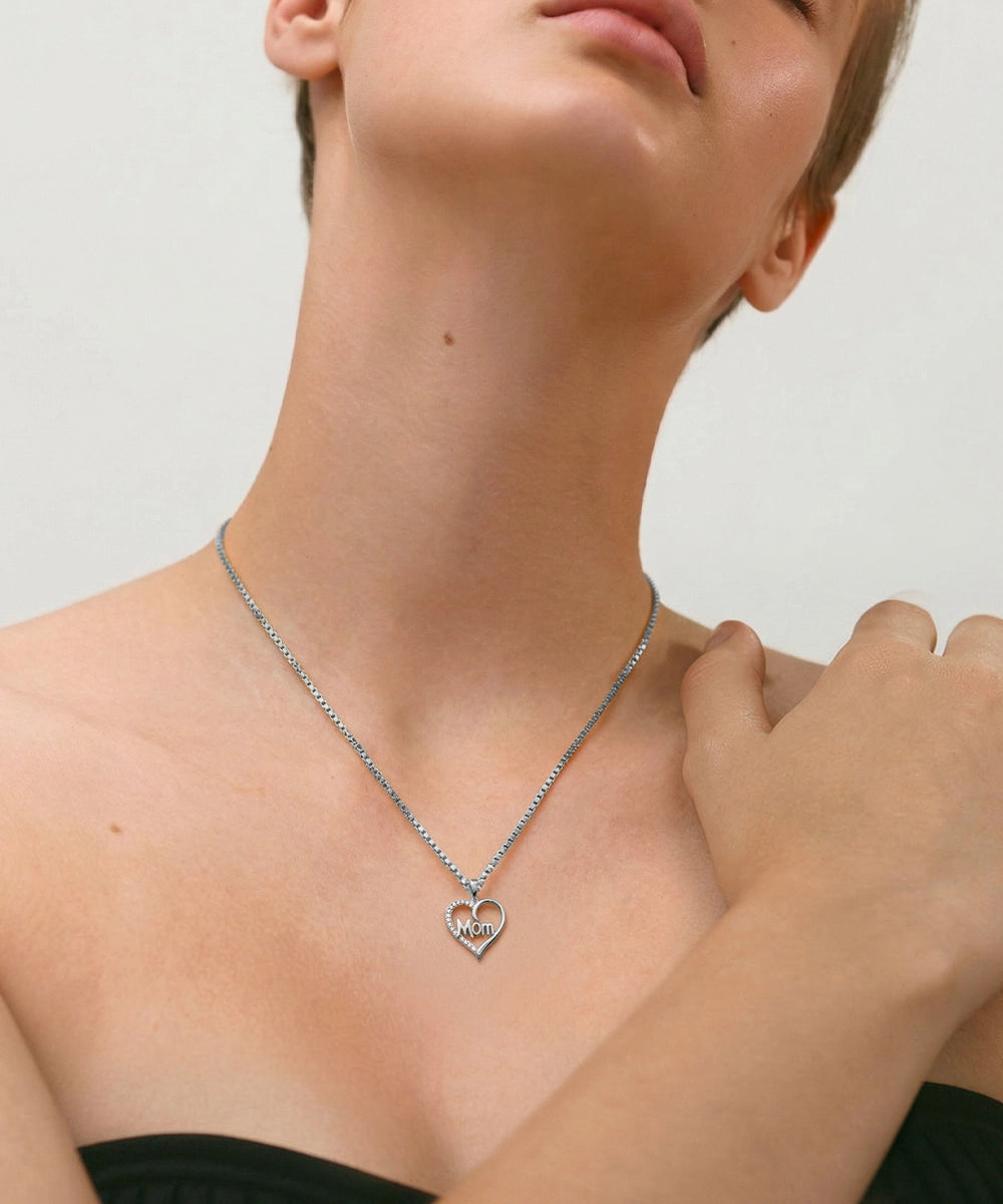 Person wearing a silver necklace with a heart pendant on a plain background