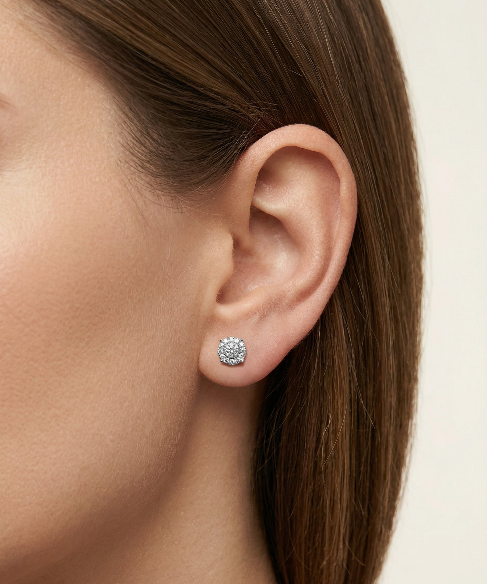 Close-up of a woman's ear wearing a sparkling earring on a neutral background