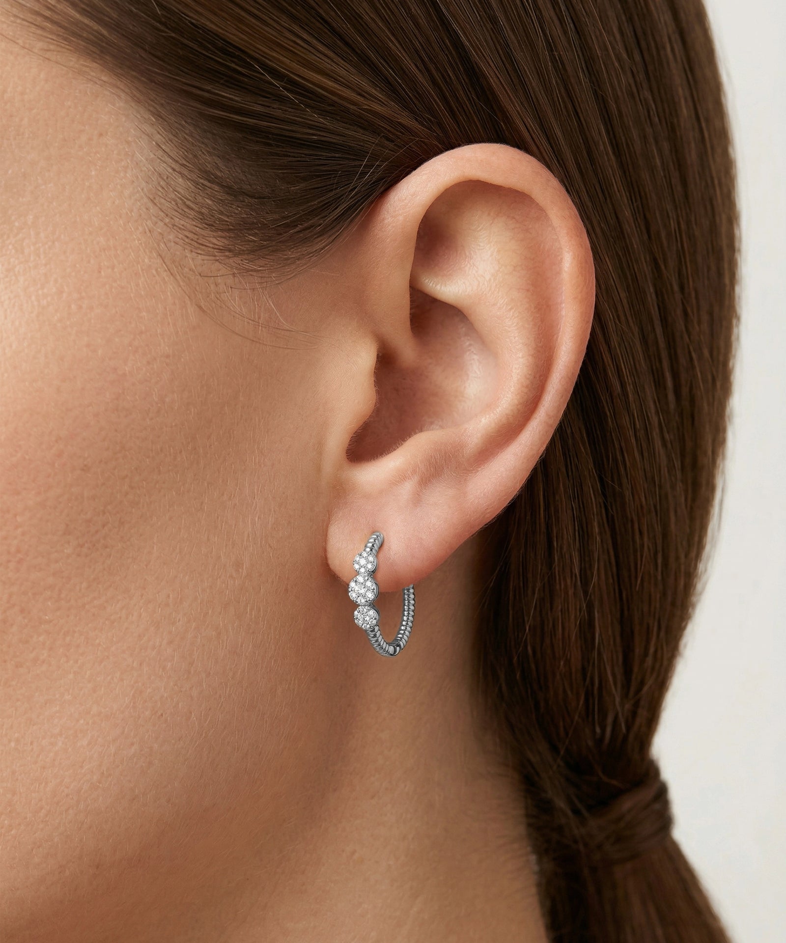 Close-up of an ear wearing a silver hoop earring with a blurred background