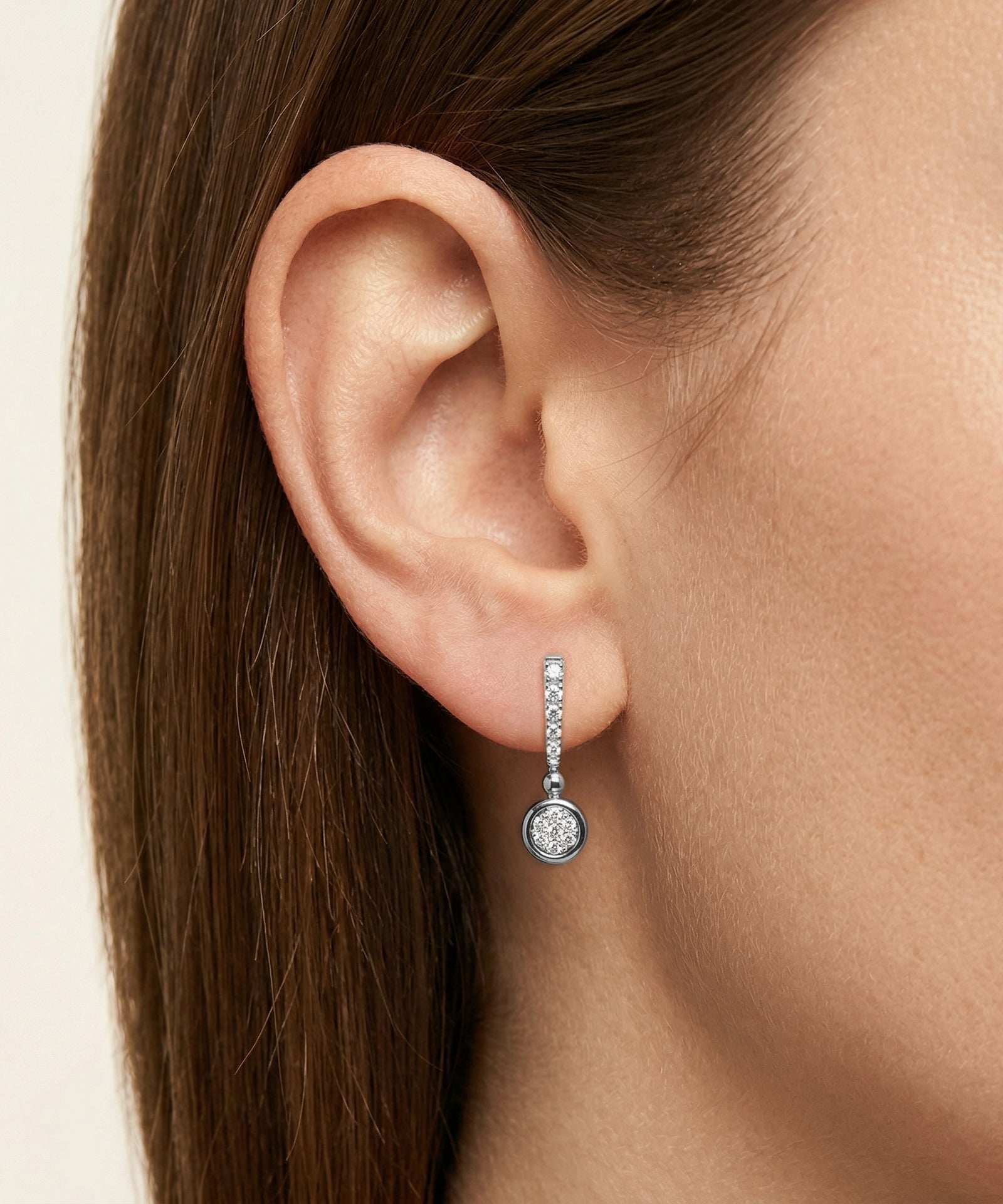Close-up of an ear wearing a diamond earring with a neutral background
