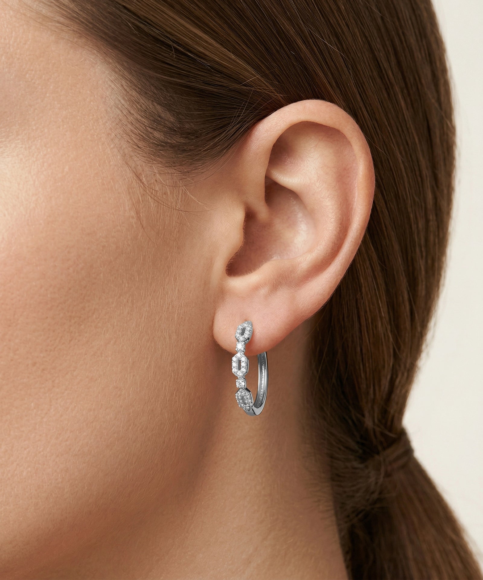 Close-up of an ear wearing a silver hoop earring with small stones.