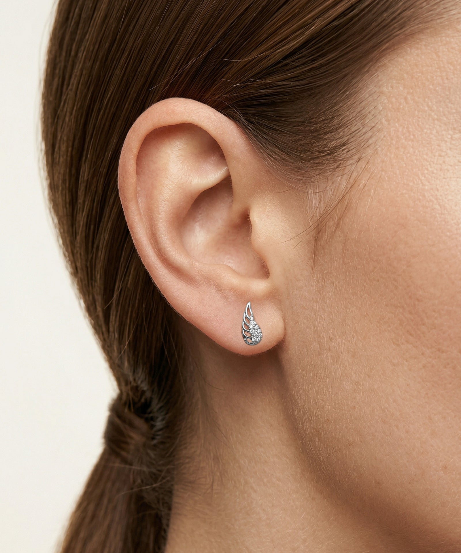 Close-up of an ear wearing a silver earring with a clear gemstone on a neutral background