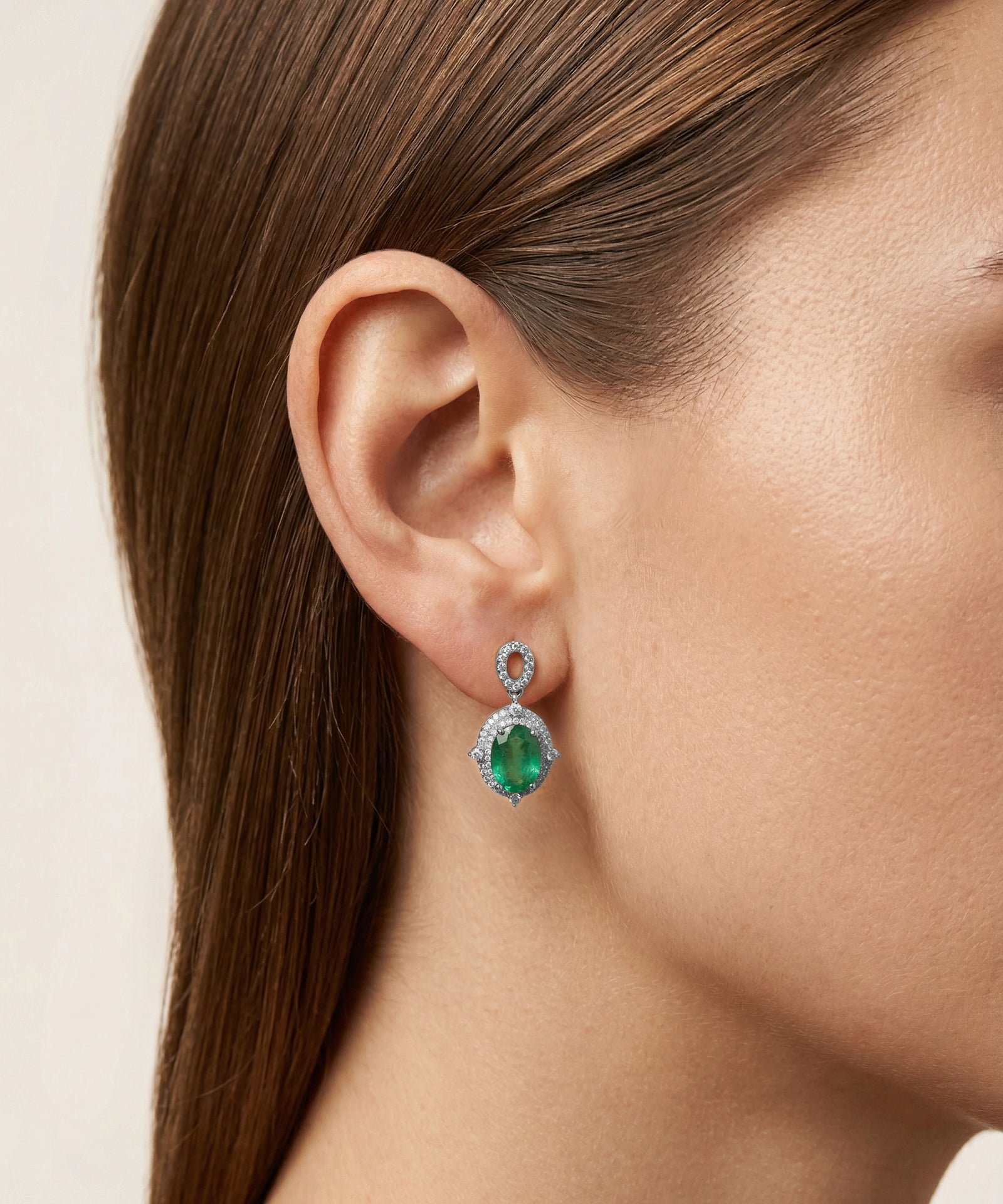Close-up of a woman wearing emerald green earrings with a beige background