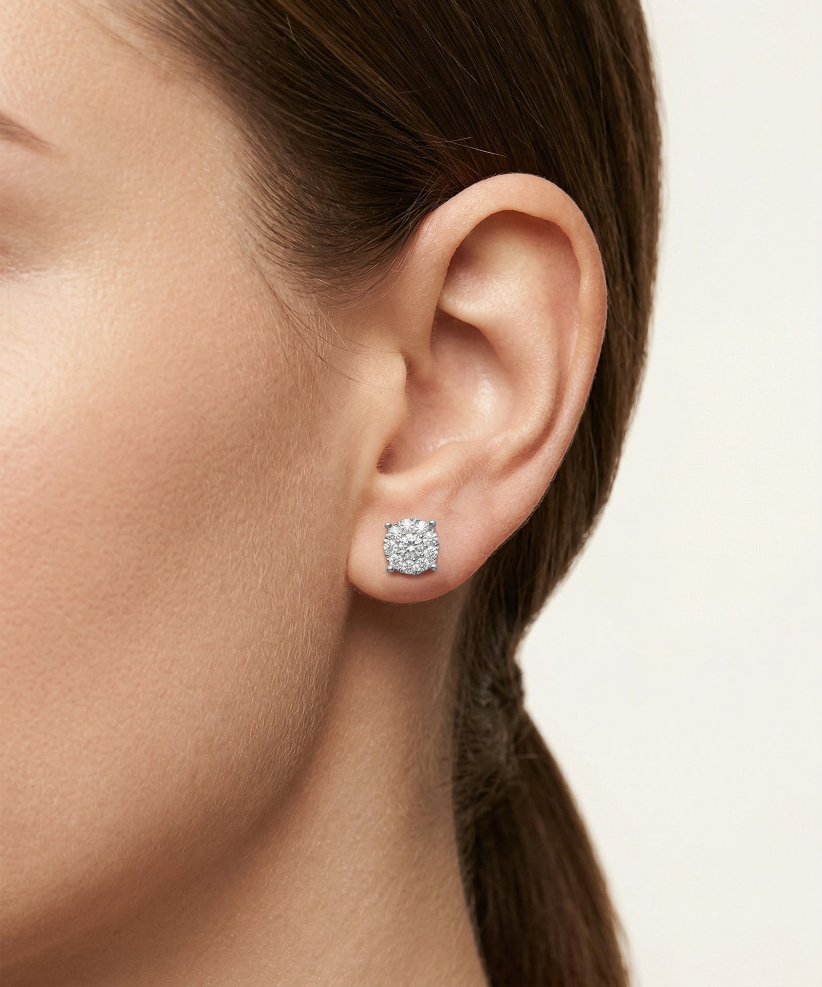 Close-up of an ear wearing a diamond stud earring with a neutral background