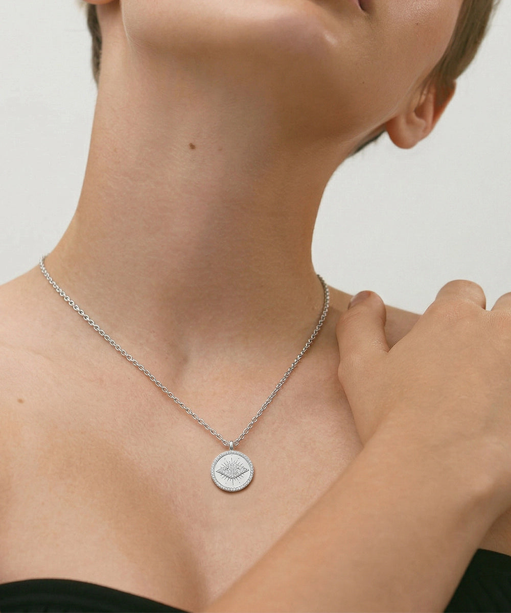 Person wearing a silver necklace with an eye pendant on a neutral background
