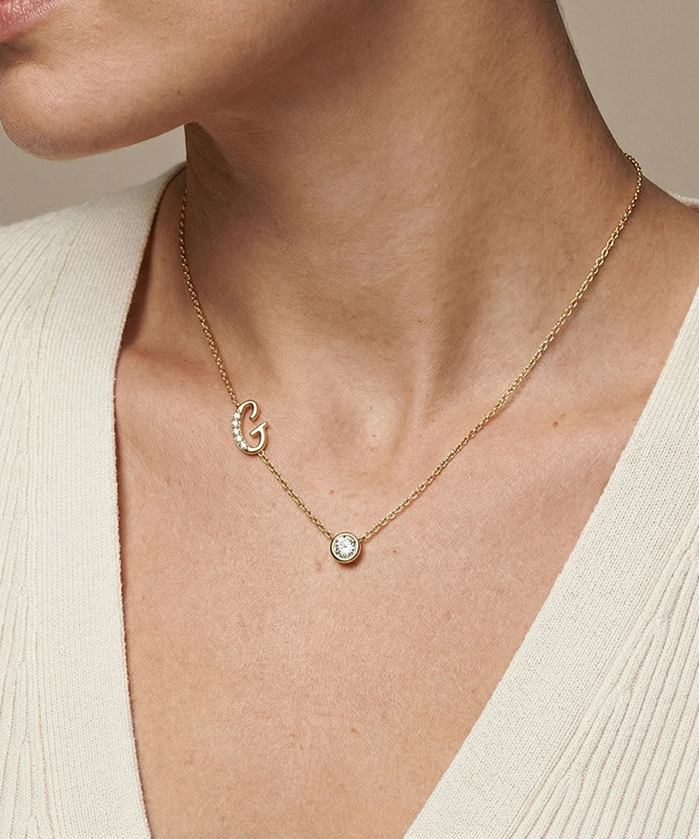 Gold necklace with a pendant on a person wearing a beige top.