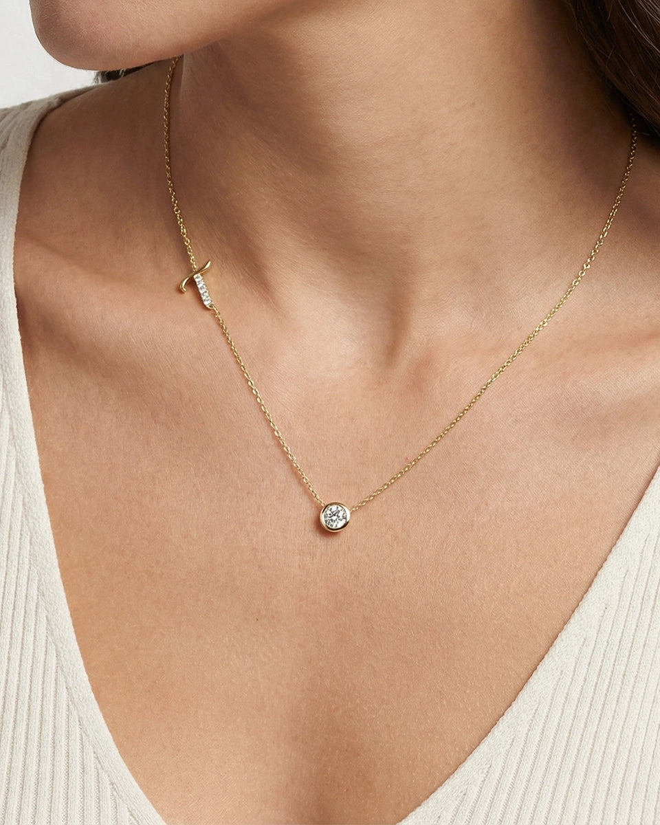 Gold necklace with a small round pendant on a person wearing a beige top.