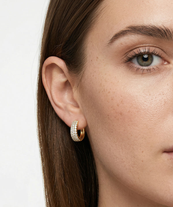 Close-up of a woman wearing gold hoop earrings with a blurred background