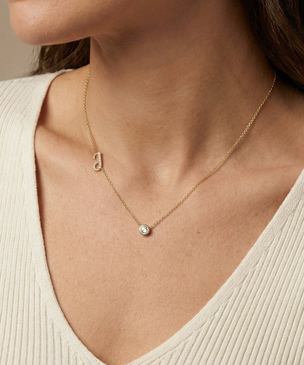 Gold necklace with a small round pendant worn by a person in a beige top.