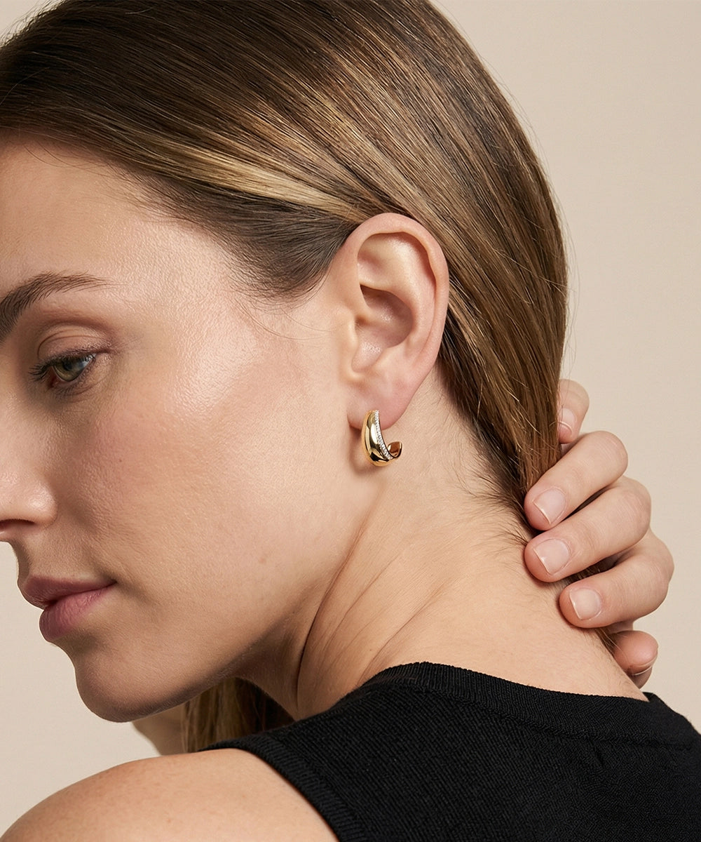 Close-up of a woman wearing gold hoop earrings with a neutral background