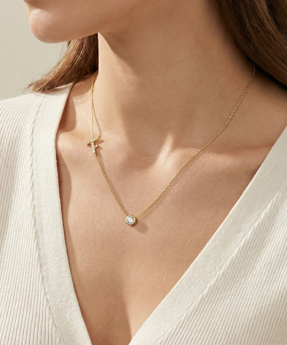 Gold necklace with a small pendant worn by a person in a white outfit.