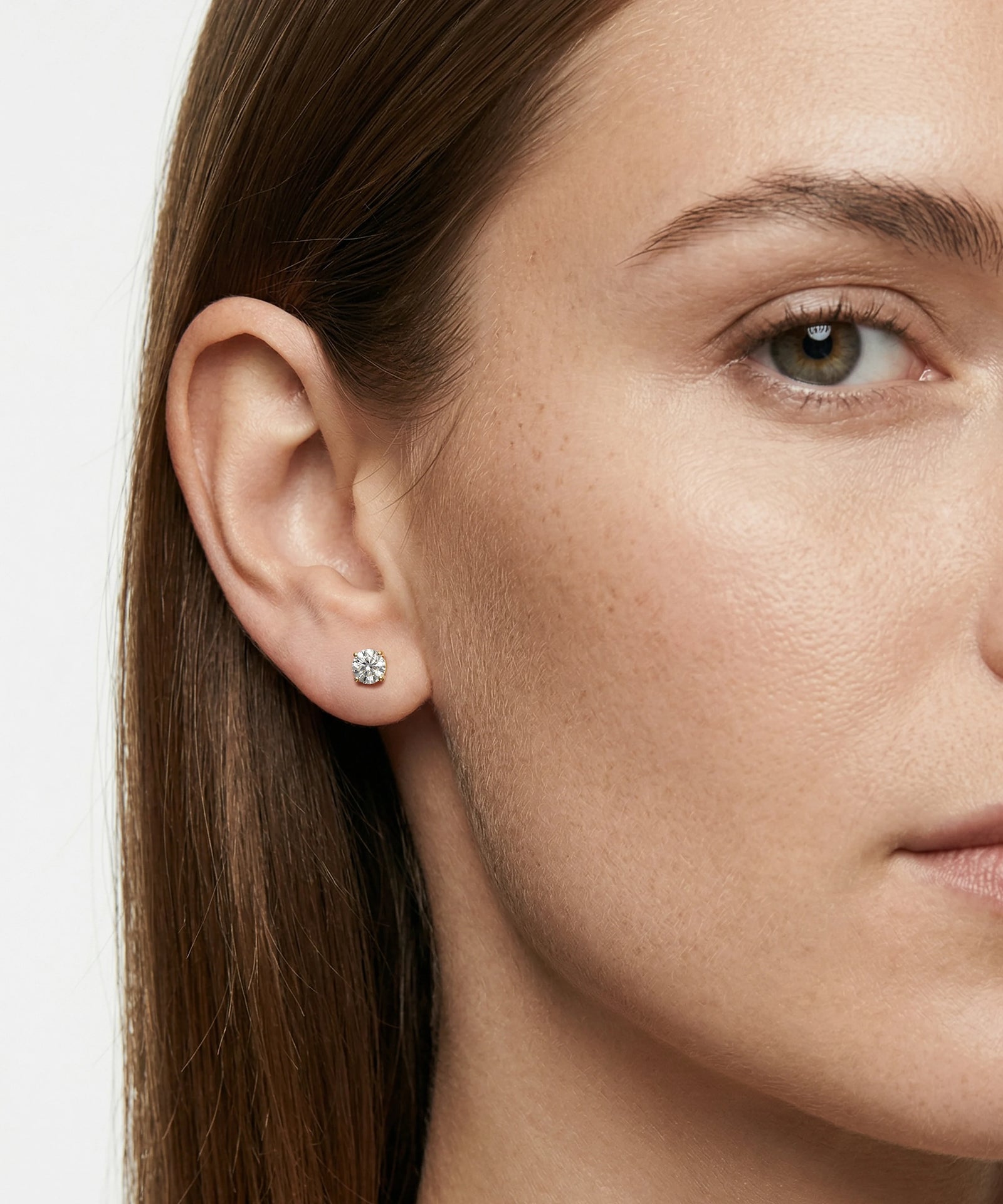 Close-up of a woman wearing diamond stud earrings with a neutral background