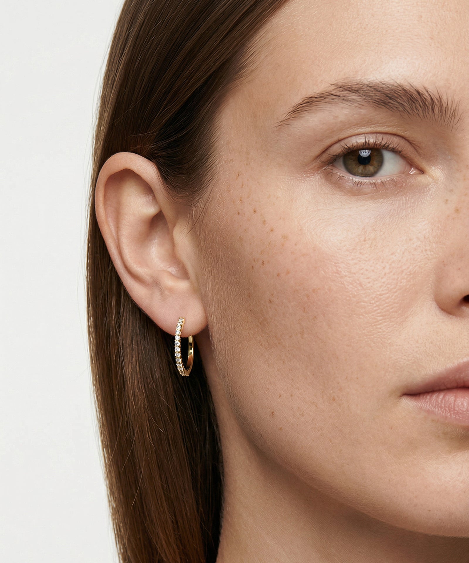 Close-up of a woman wearing gold hoop earrings with a plain background