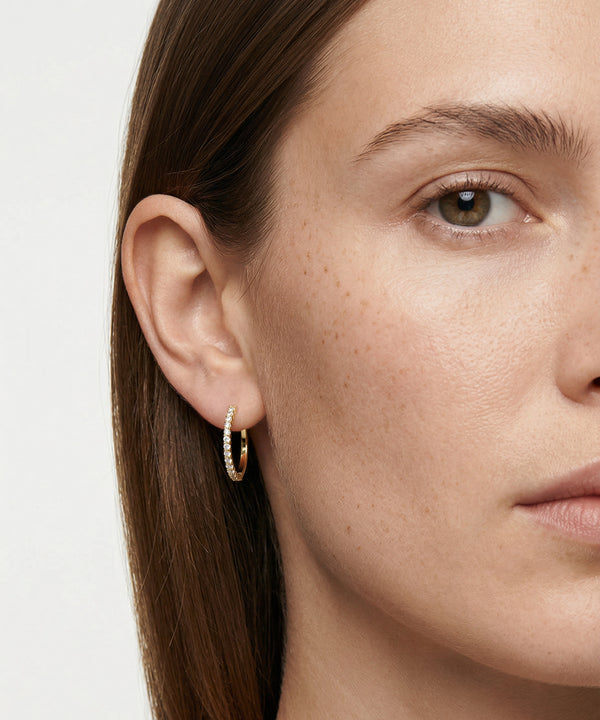 Close-up of a woman wearing gold hoop earrings with a plain background