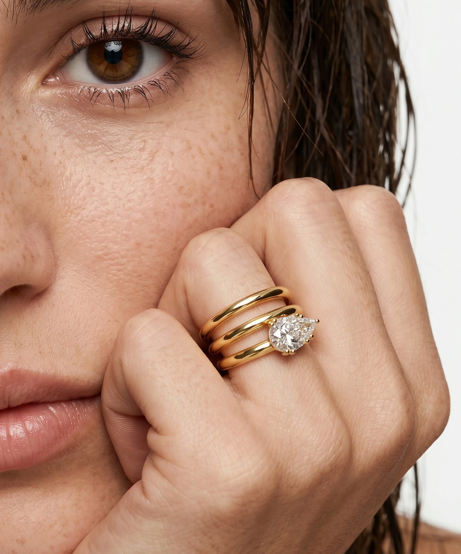Close-up of a woman's face with a hand holding a diamond ring.