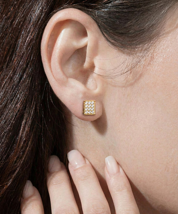 Close-up of an ear wearing a diamond stud earring with a hand touching the cheek.
