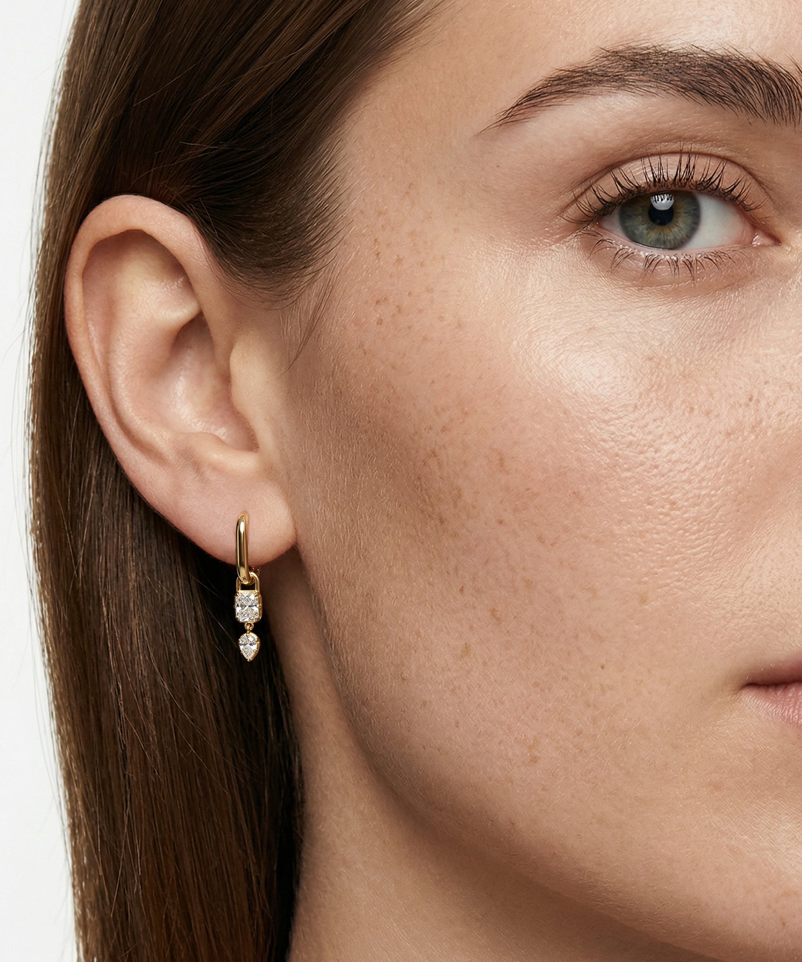 Close-up of a woman's ear wearing gold earrings with a white stone.