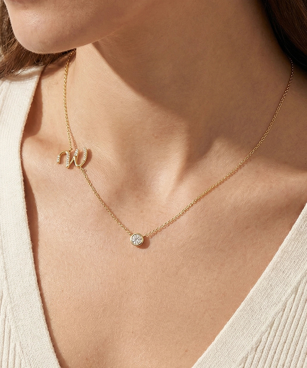 Gold necklace with a small round pendant on a person wearing a beige top.