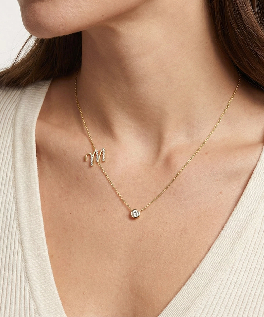 Gold necklace with a letter 'M' pendant worn by a person