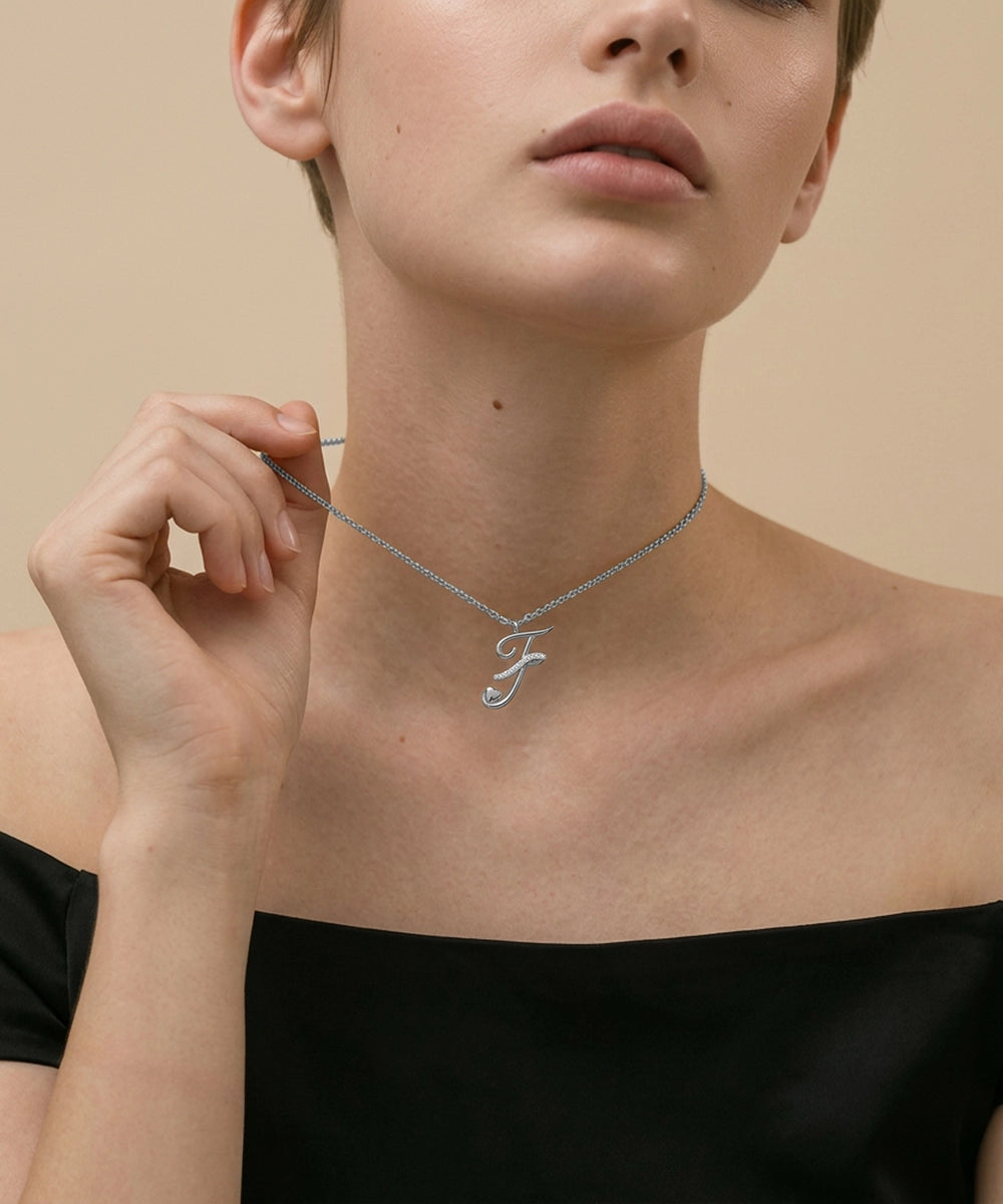 Person wearing a silver necklace with a letter 'S' pendant on a beige background