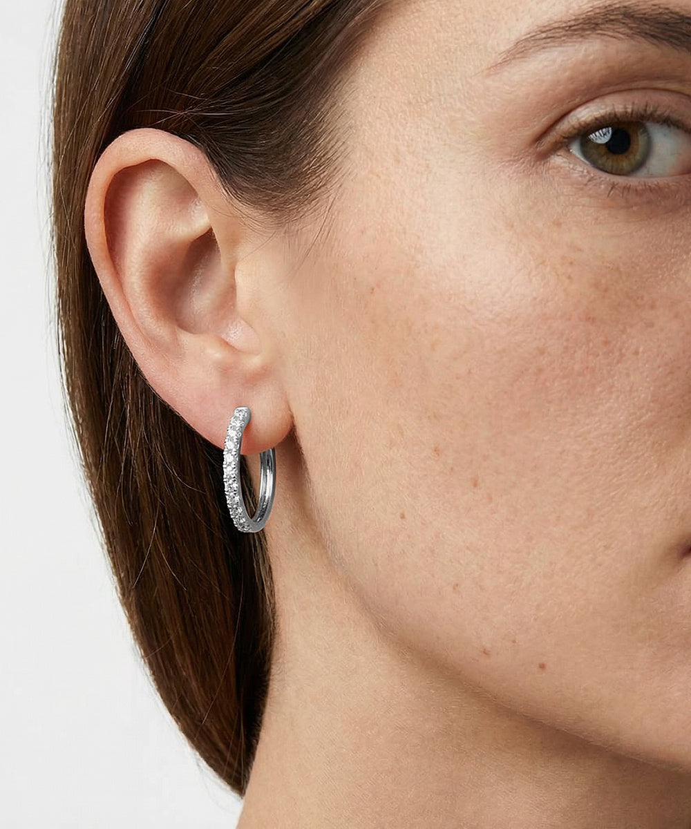 Close-up of a person wearing a silver hoop earring with a white background