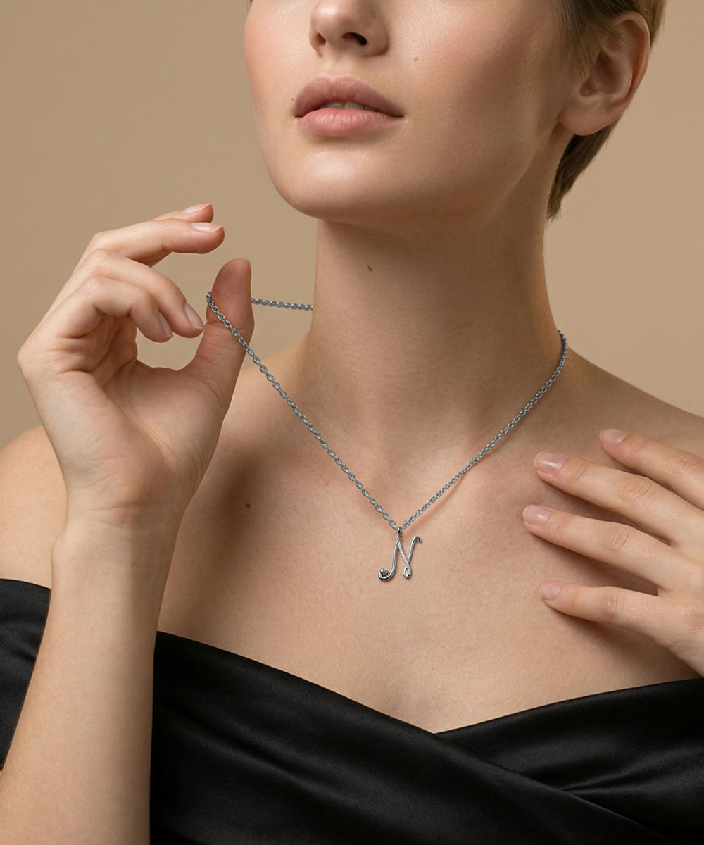 Woman wearing a silver necklace with a letter 'N' pendant against a beige background