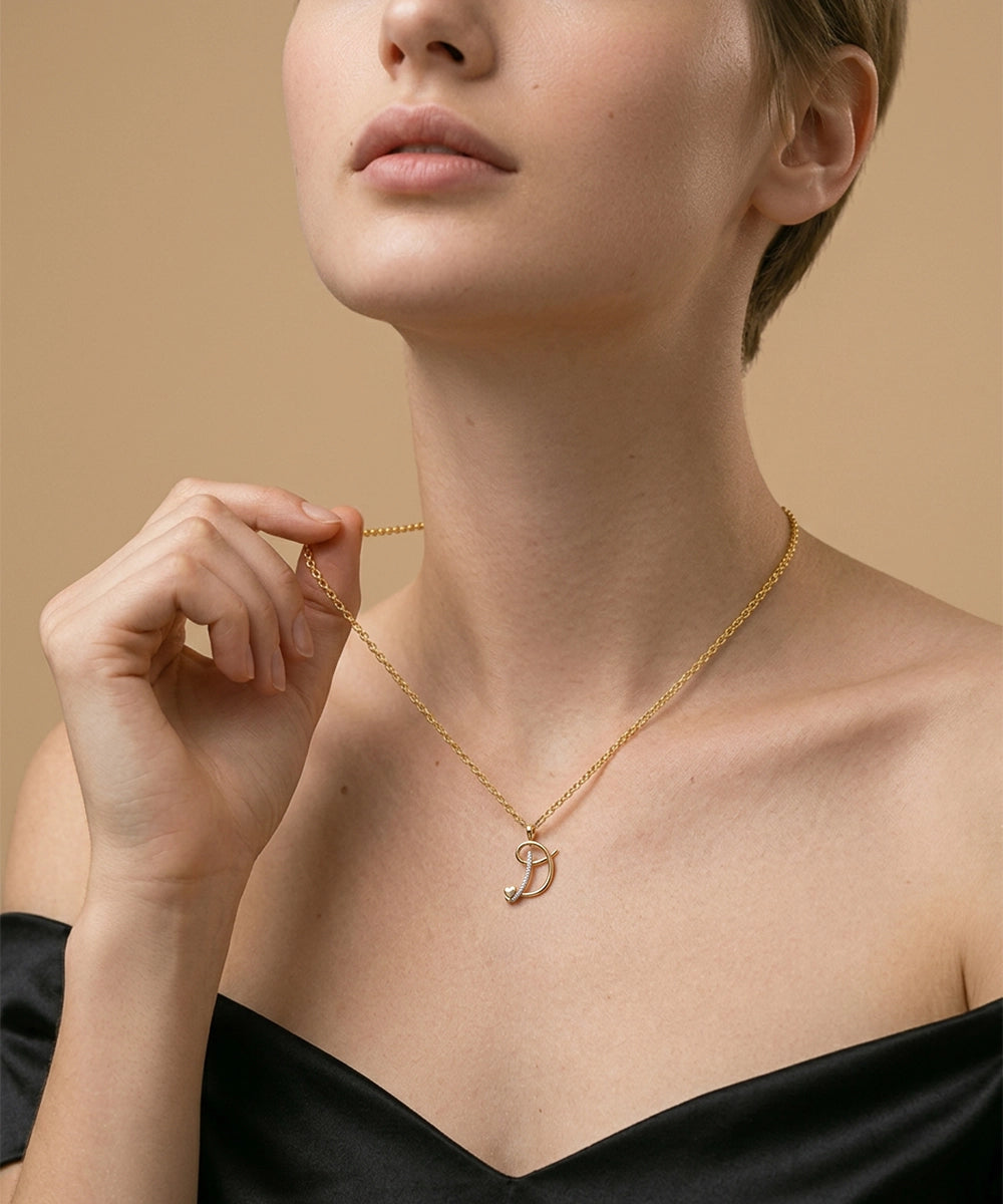 Woman wearing a gold necklace with a 'D' pendant against a beige background