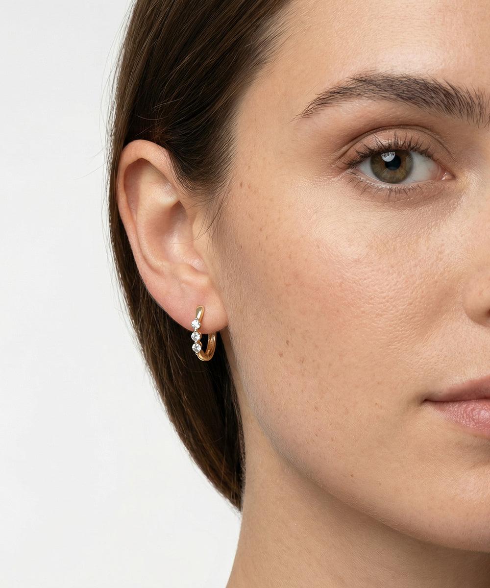 Close-up of a woman wearing a gold hoop earring with small pearls on a plain background