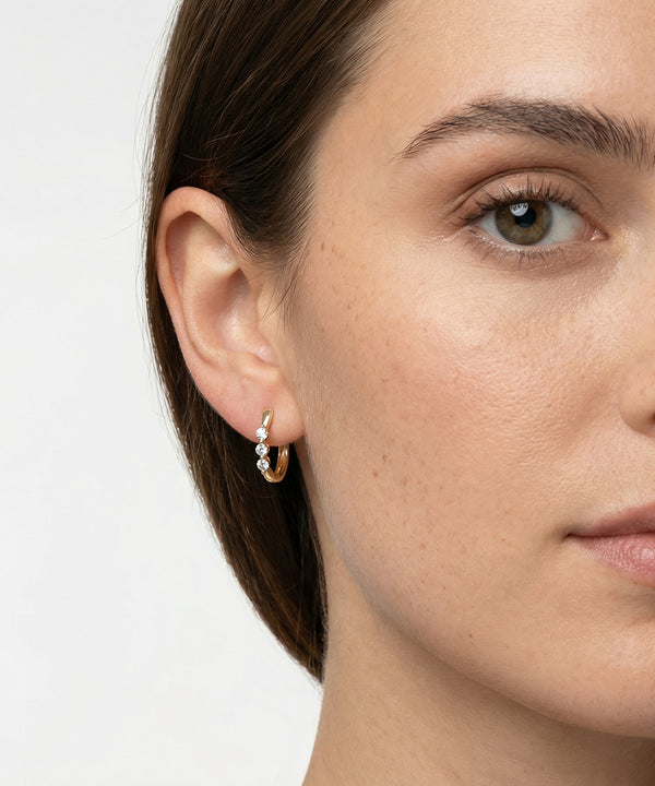 Close-up of a woman wearing a gold hoop earring with small pearls on a plain background