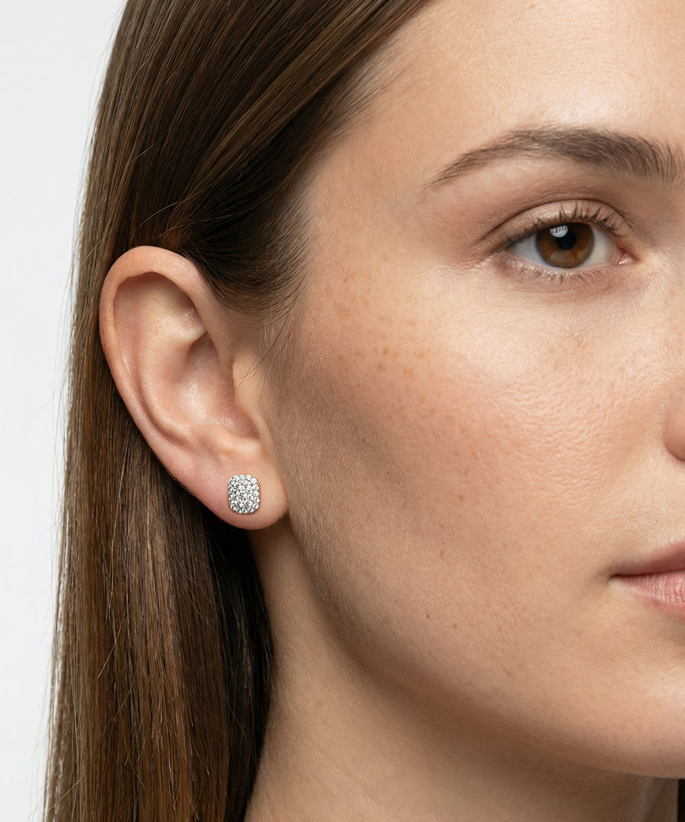 Close-up of a woman wearing diamond stud earrings with a plain background