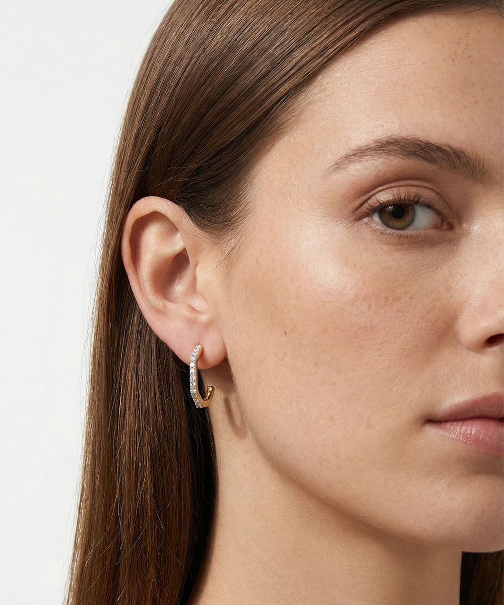 Close-up of a woman wearing a gold hoop earring on a plain background
