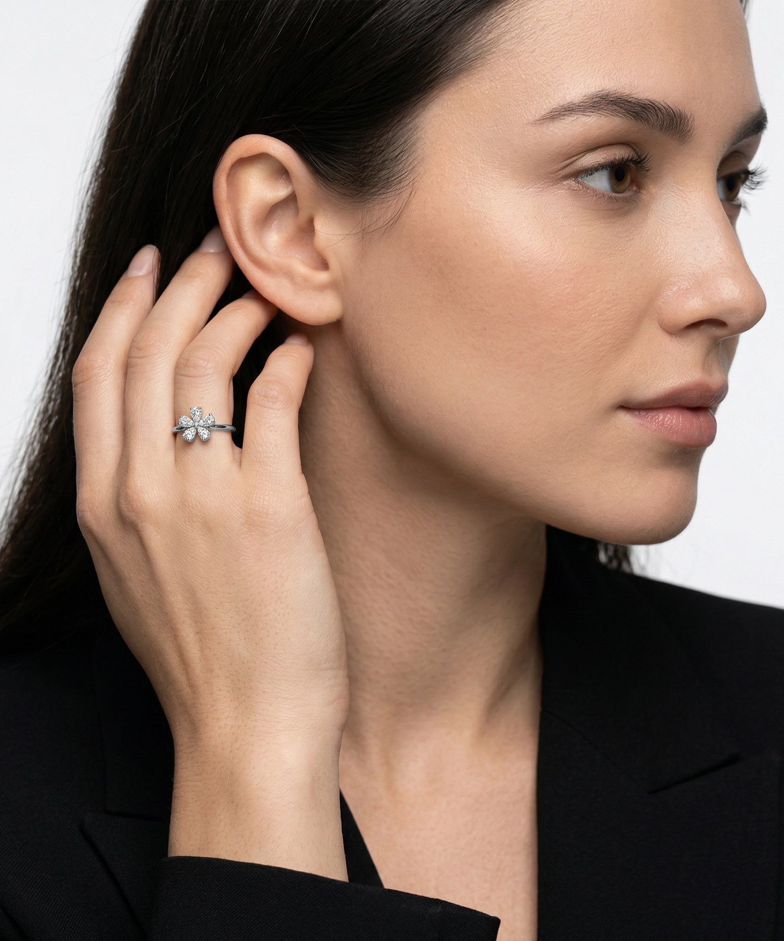 Woman wearing a ring with a diamond, touching her ear against a neutral background