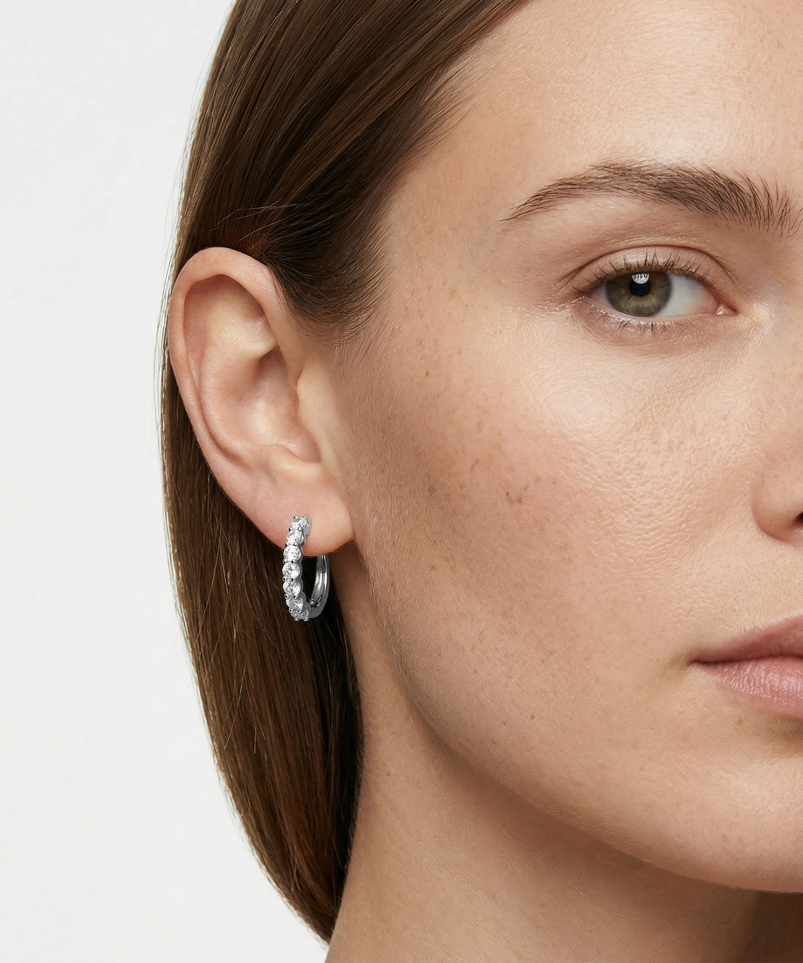 Close-up of a woman wearing silver hoop earrings with a neutral background