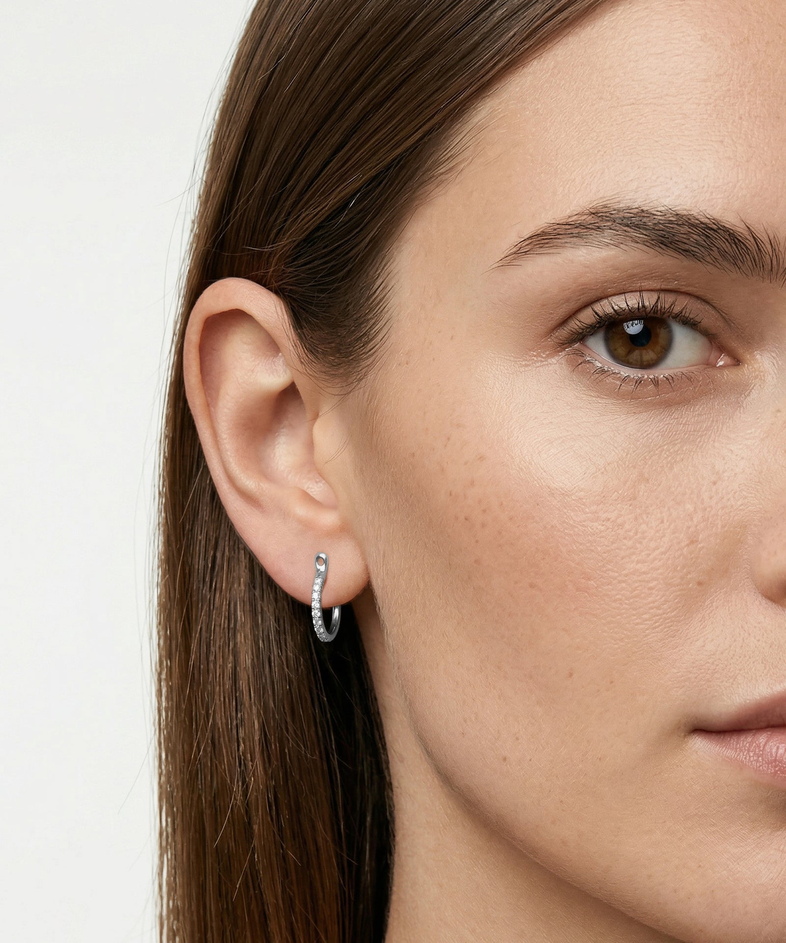 Close-up of a woman wearing a silver hoop earring against a neutral background