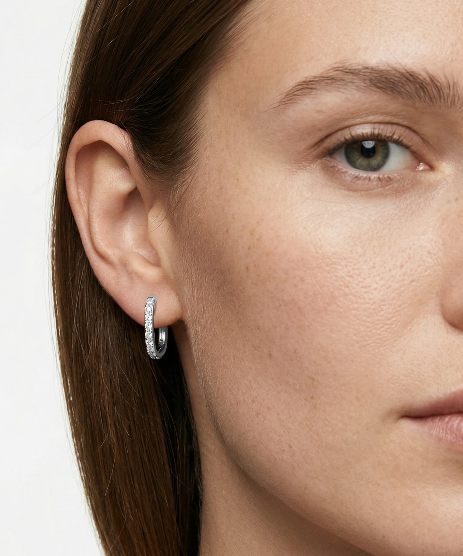 Close-up of a woman wearing silver hoop earrings with a neutral background