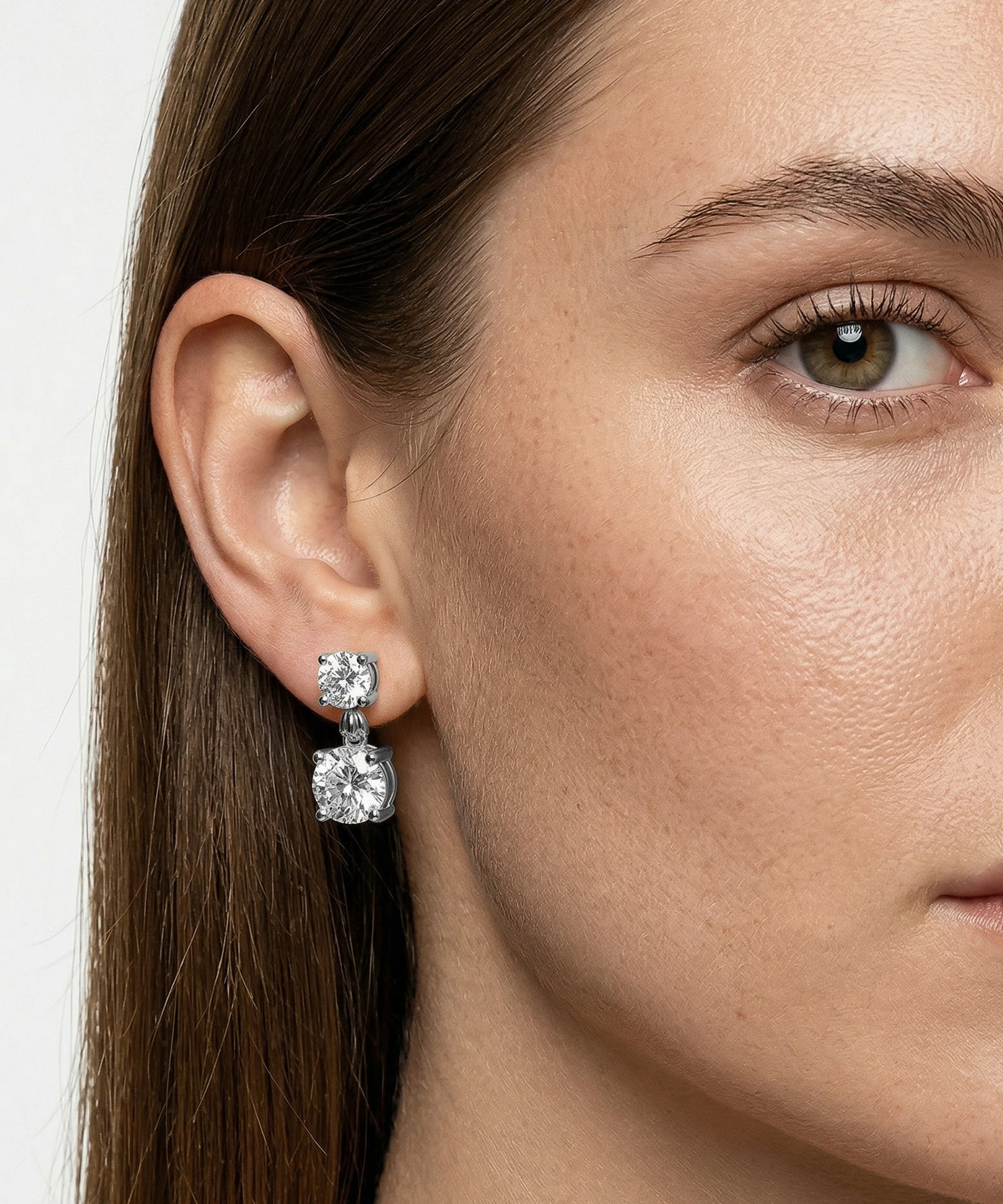 Close-up of a woman wearing diamond earrings with a plain background